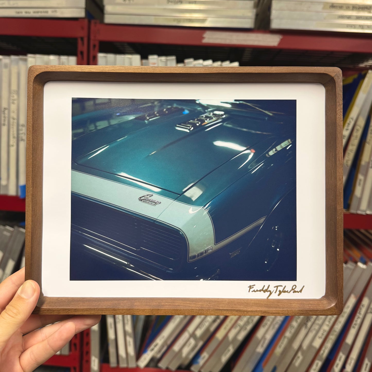 Framed picture of a blue car held in front of bookshelves