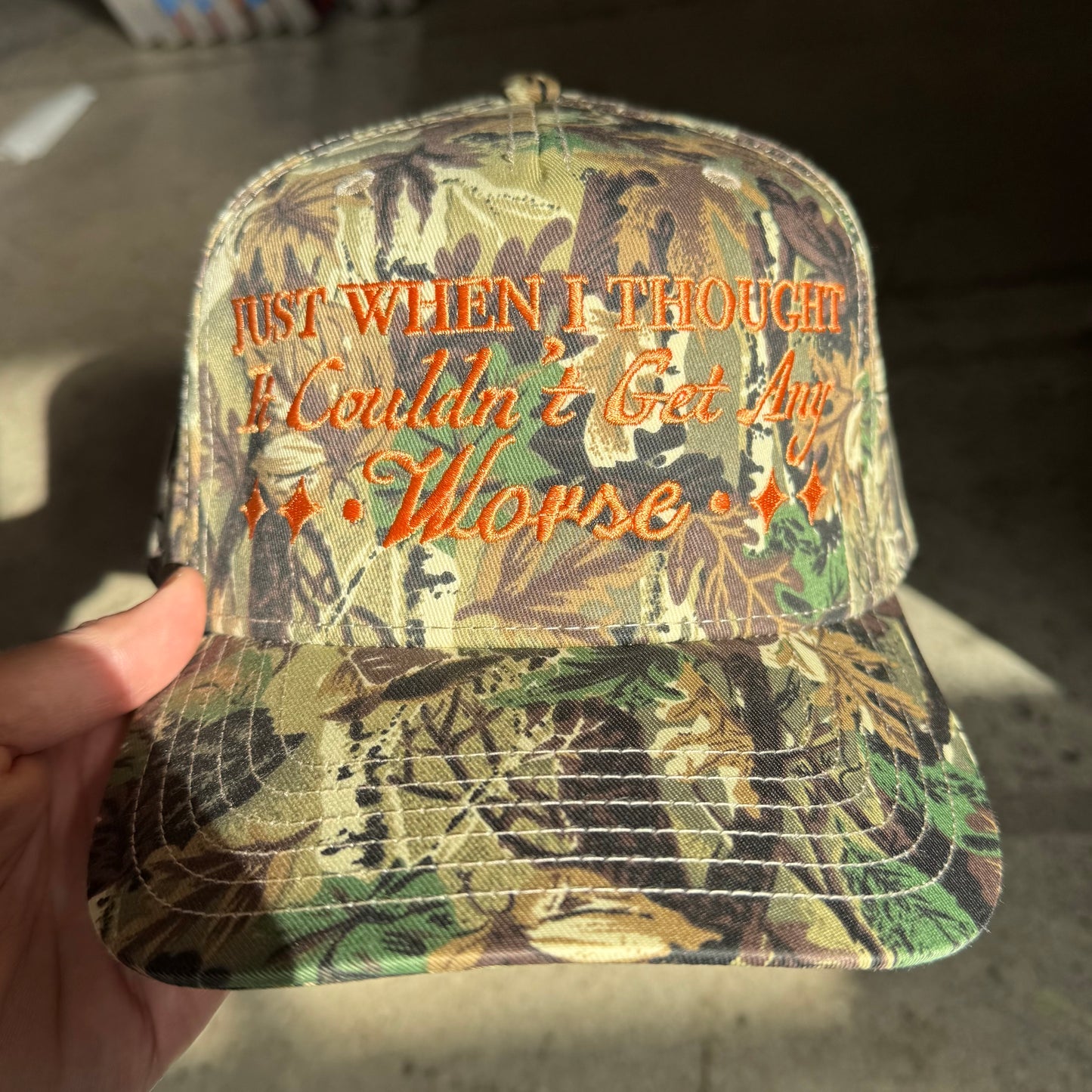 Camouflage cap with text held by a hand on a neutral background