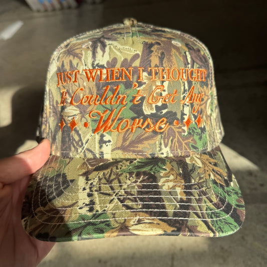 Camouflage cap with text held by a hand on a neutral background