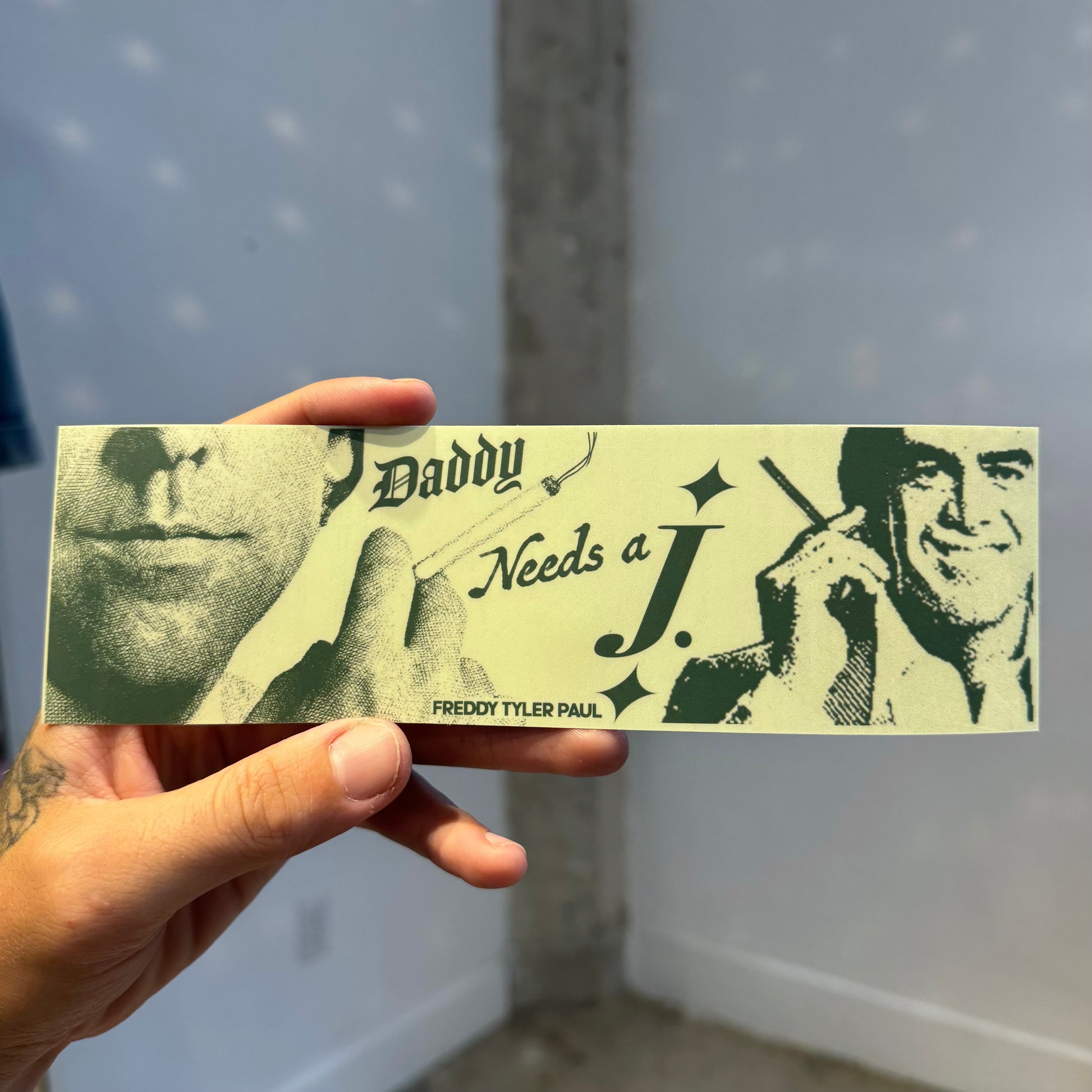 Hand holding a product with 'Daddy Needs a J.' text and images of two men smoking.