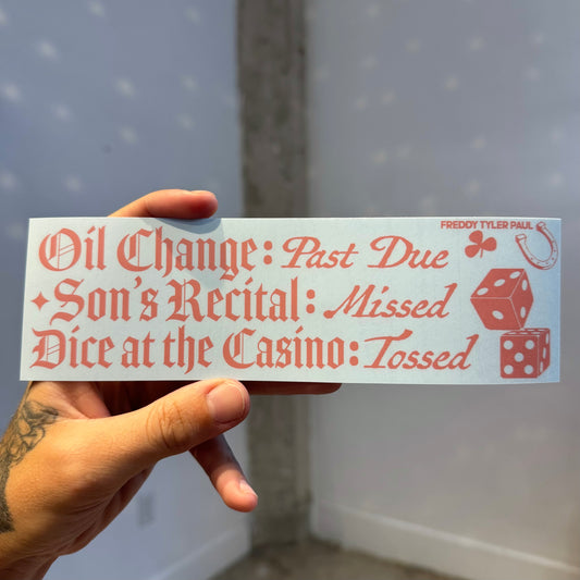 Hand holding a humorous bumper sticker with text and dice graphics.