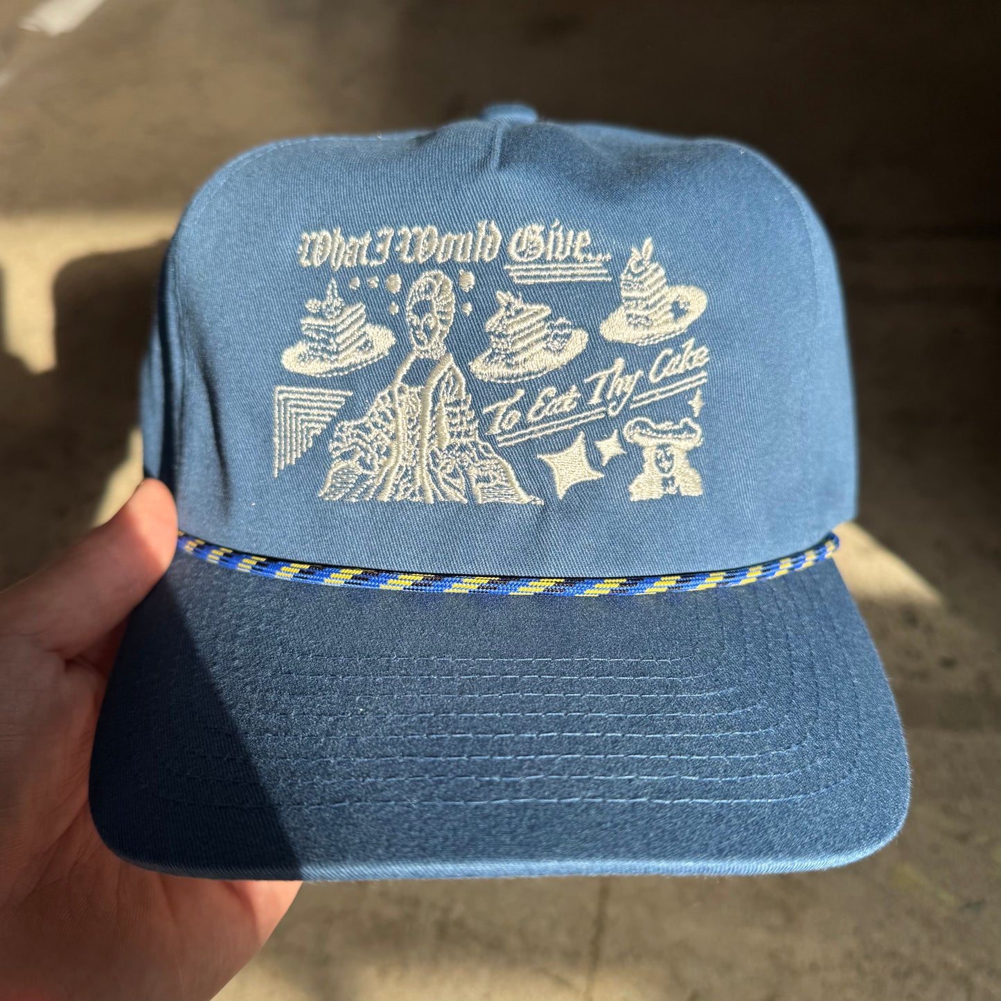 Blue cap with white text and graphics held by a hand against a blurred background