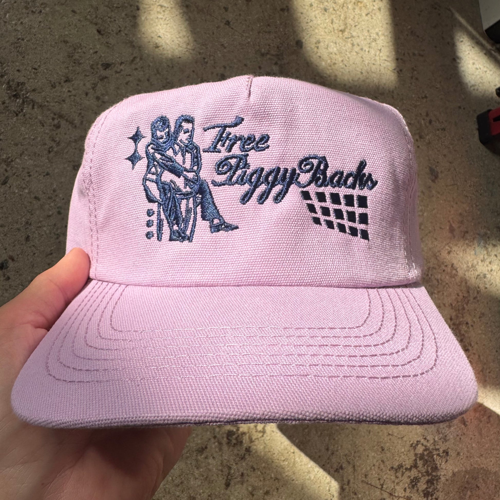 Pink cap with embroidered design held by a hand on a concrete surface