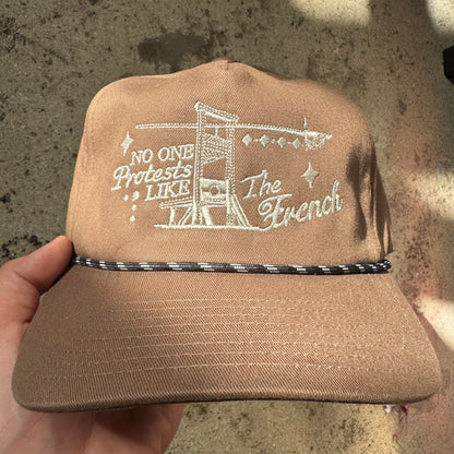 Brown cap with white embroidered text held against a concrete background