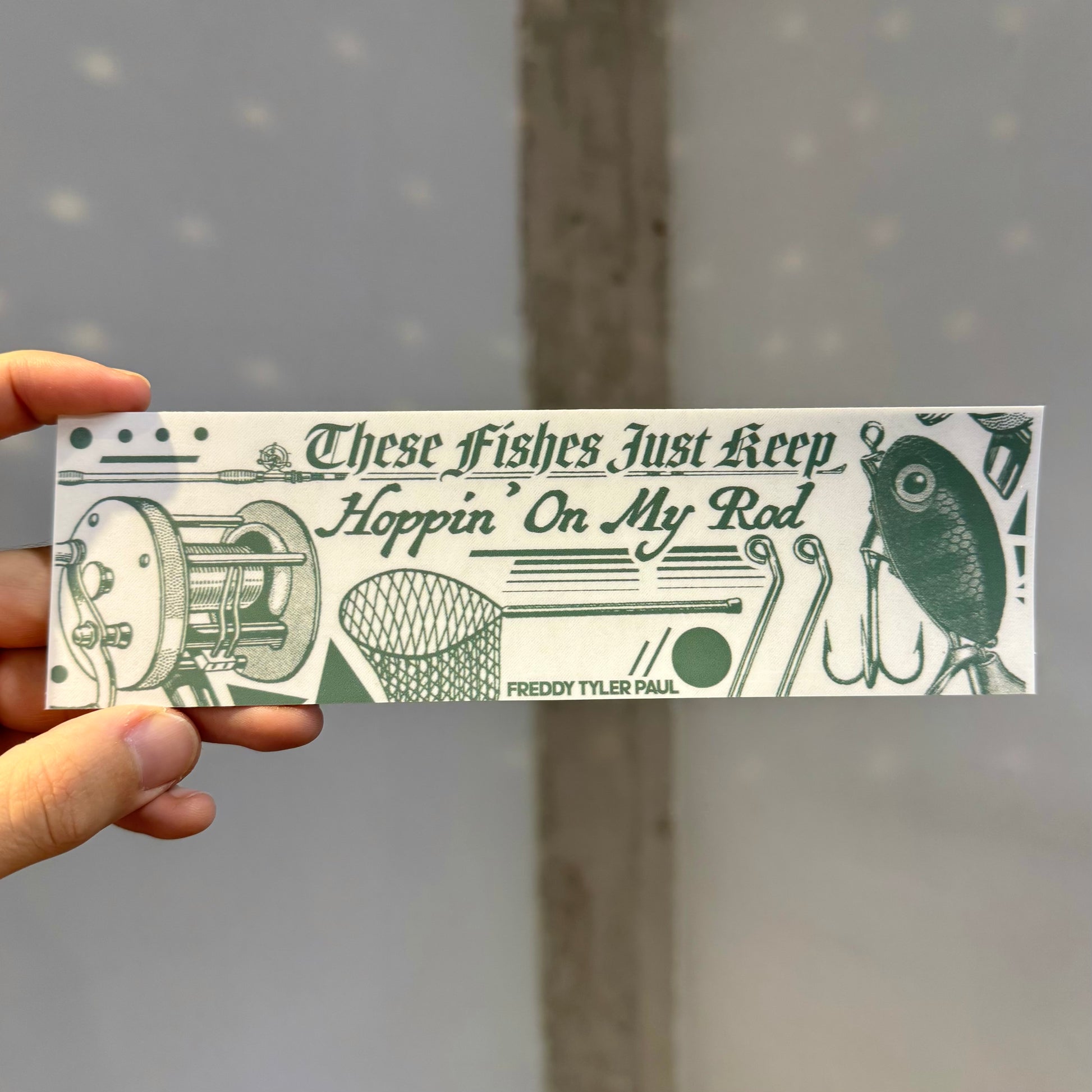 Hand holding a printed strip with fishing-themed design and text.