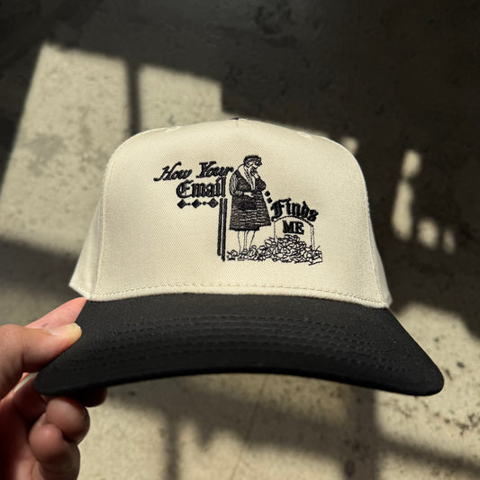 Trucker hat with black and white graphic design held by a hand on a textured surface.
