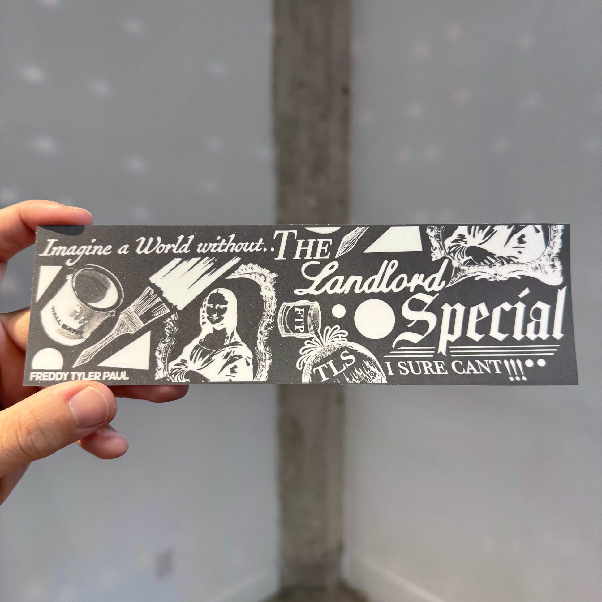 Hand holding a black and white sticker with text and graphics against a gray background