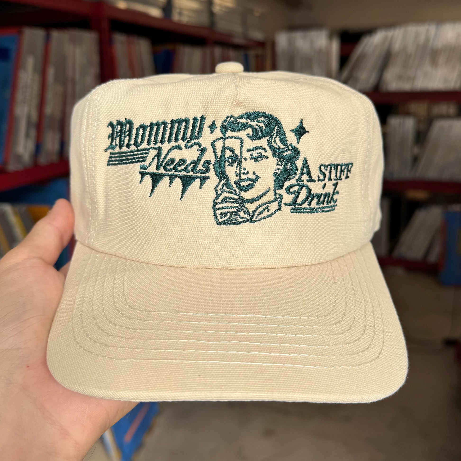 Beige cap with text and graphic held in front of a shelf with records.