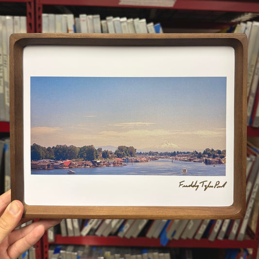 Framed photograph of a scenic view with a signature held in front of a bookshelf.
