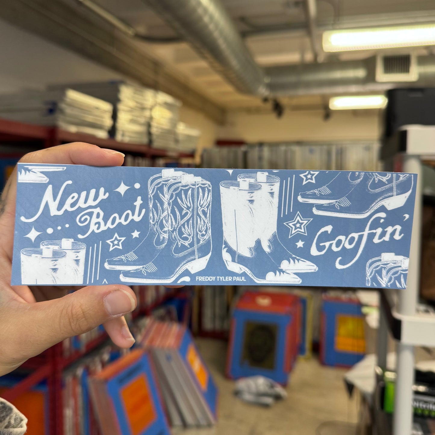 Card with cowboy boots design held in front of a bookshelf