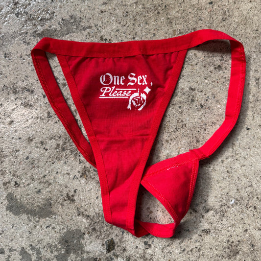 Red thong with 'One Sex Please' text on a concrete surface