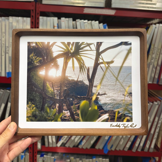 Framed photograph of a tropical beach scene held in front of a bookshelf.