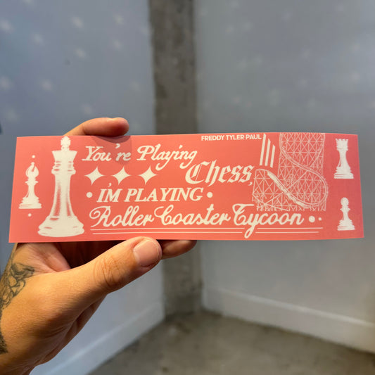 Hand holding a red bumper sticker with chess-themed text and graphics.