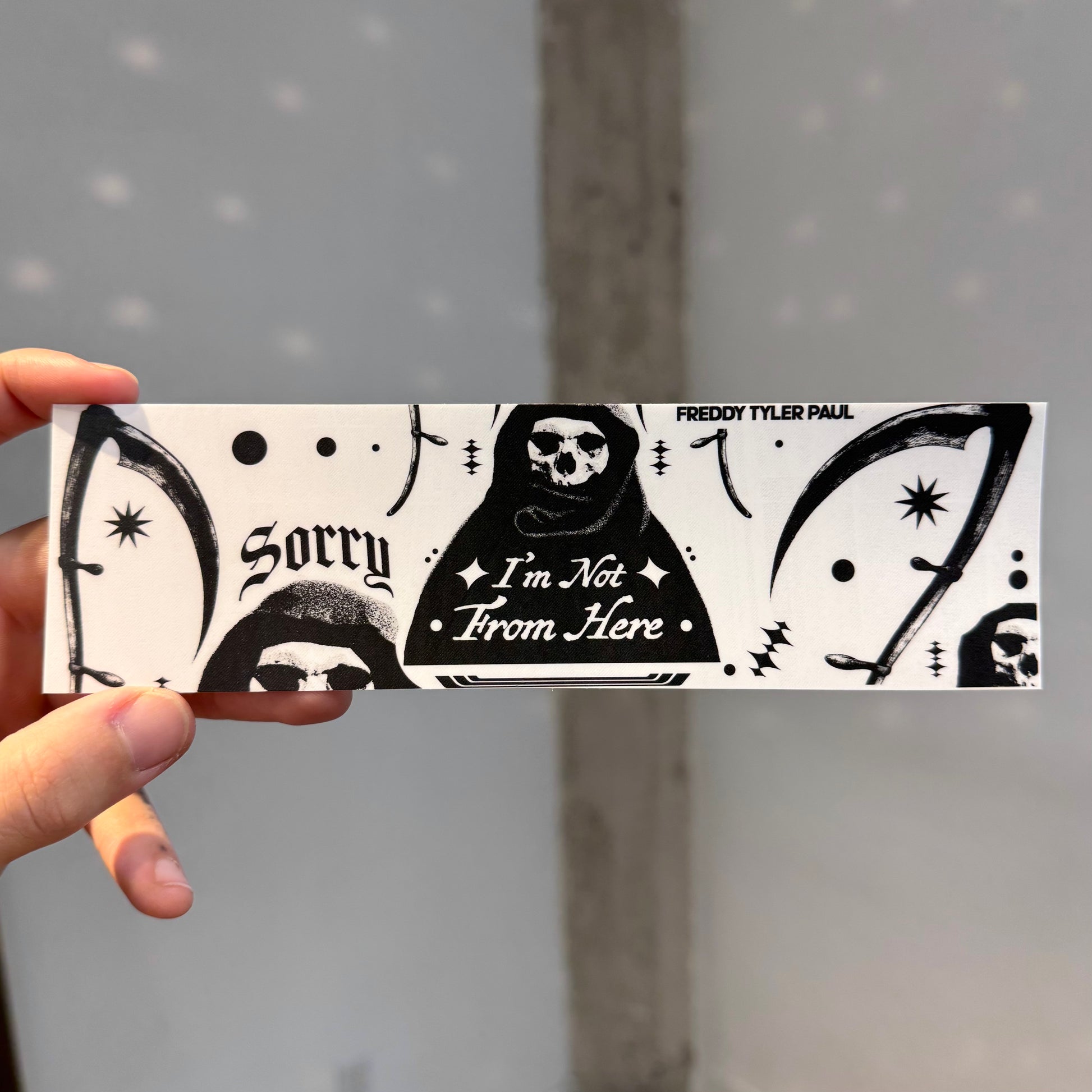 Hand holding a black and white bumper sticker with text and design elements.