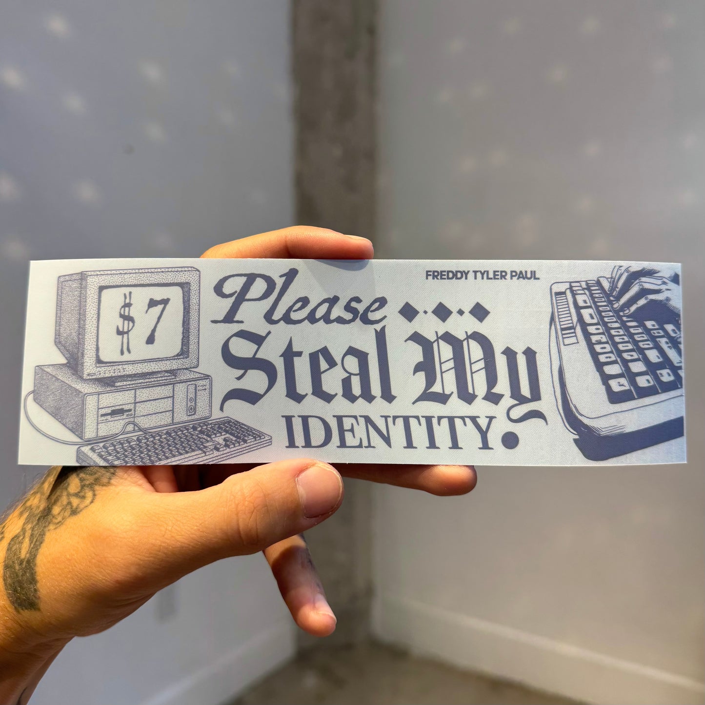 Hand holding a 'Please Steal My Identity' sticker with vintage computer graphics.