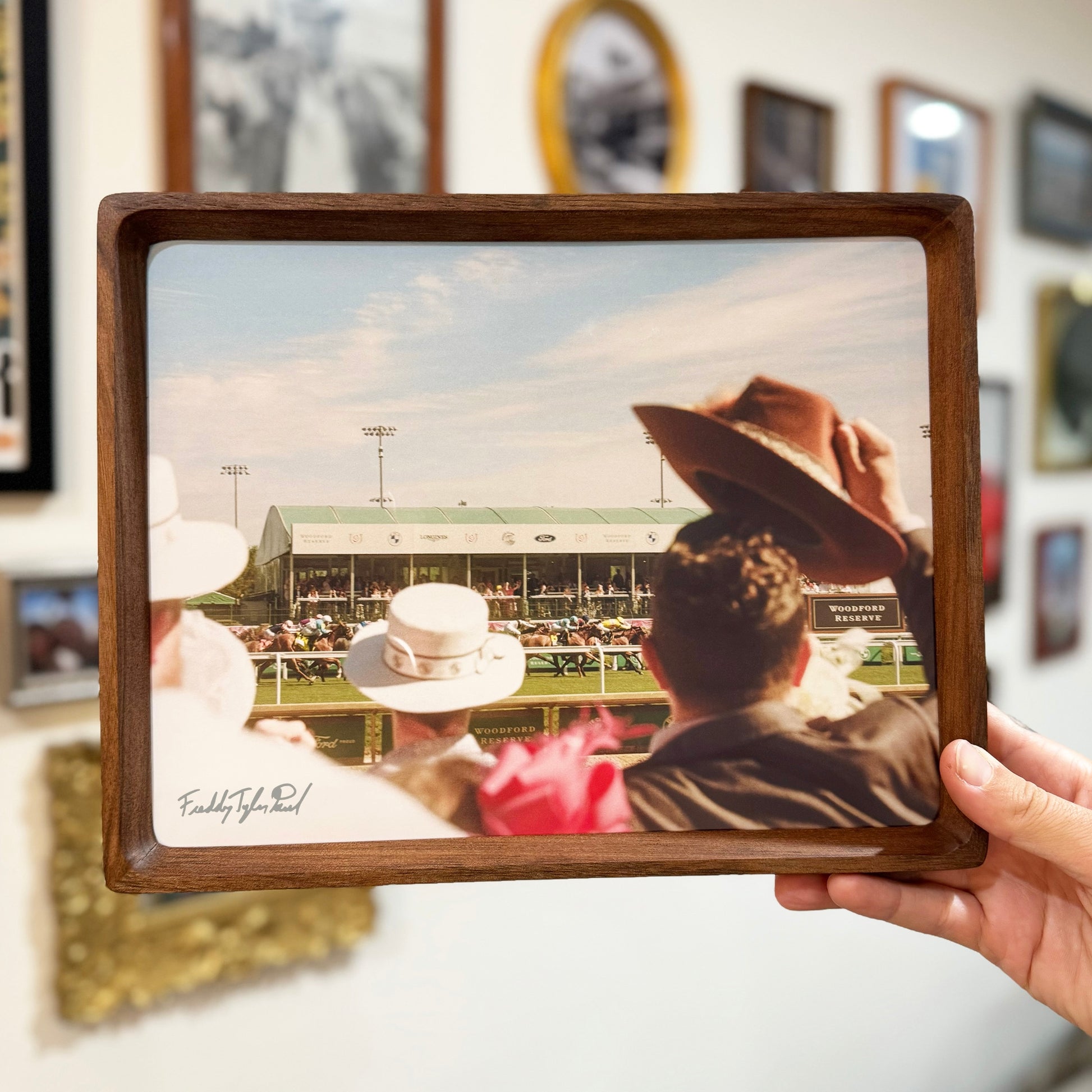 Person holding a wooden-framed photograph of people at a race track.