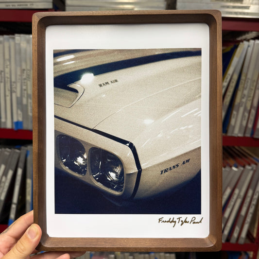 Framed picture of a car's headlight held in front of a bookshelf.