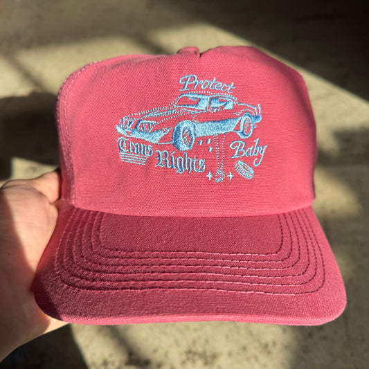 Red cap with blue text and car graphic held by a hand on a blurred background