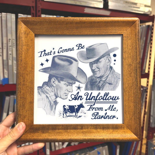Framed picture with a black and white illustration of two cowboys and text, held in front of a bookshelf.
