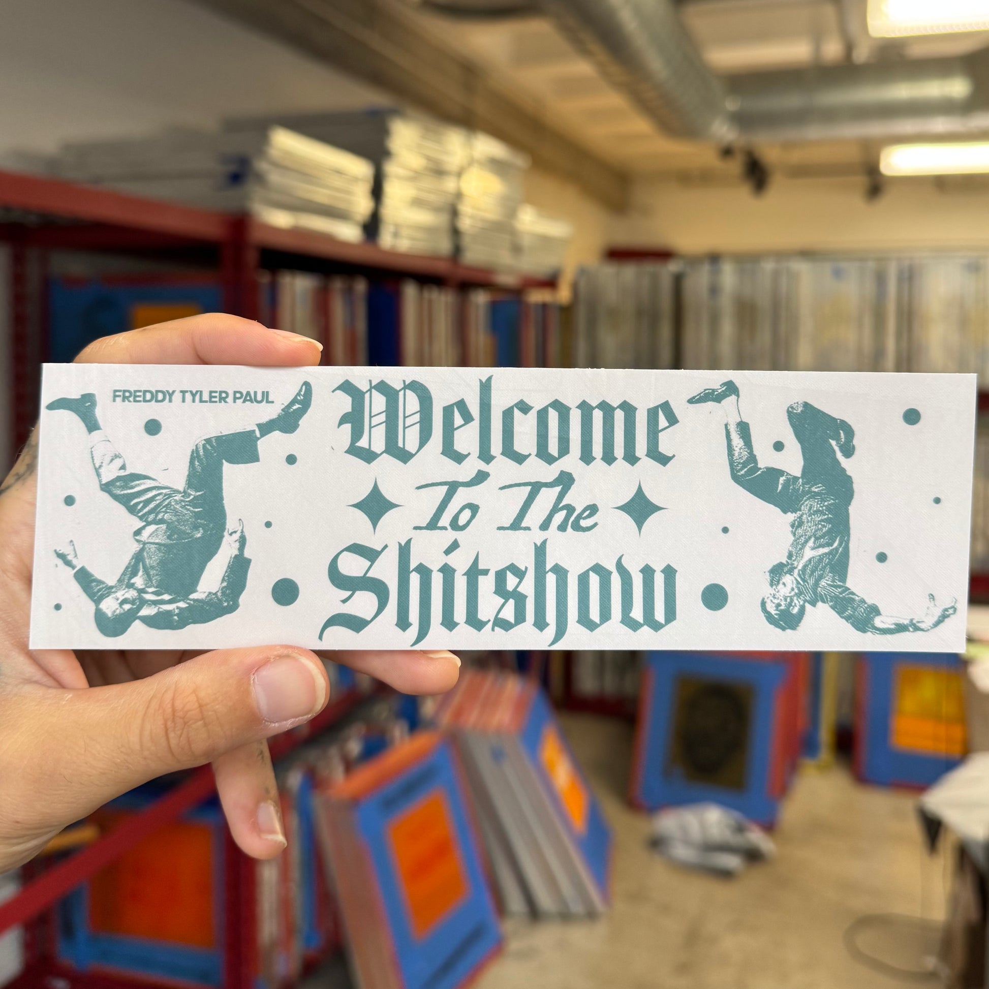 Hand holding a bumper sticker with text and graphics in a library setting