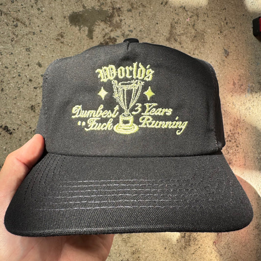 Black cap with yellow text held by a hand on a concrete surface