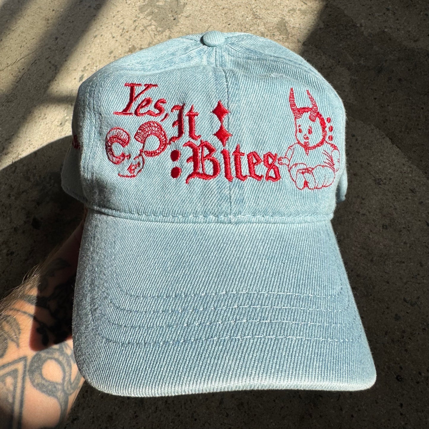 Light blue cap with red embroidered text and design on a concrete surface